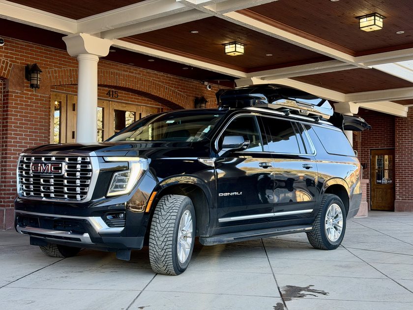 Blue Sky Limo GMC Yukon Denali XL with rooftop cargo box at a downtown Aspen hotel, ready for an Aspen airport transfer