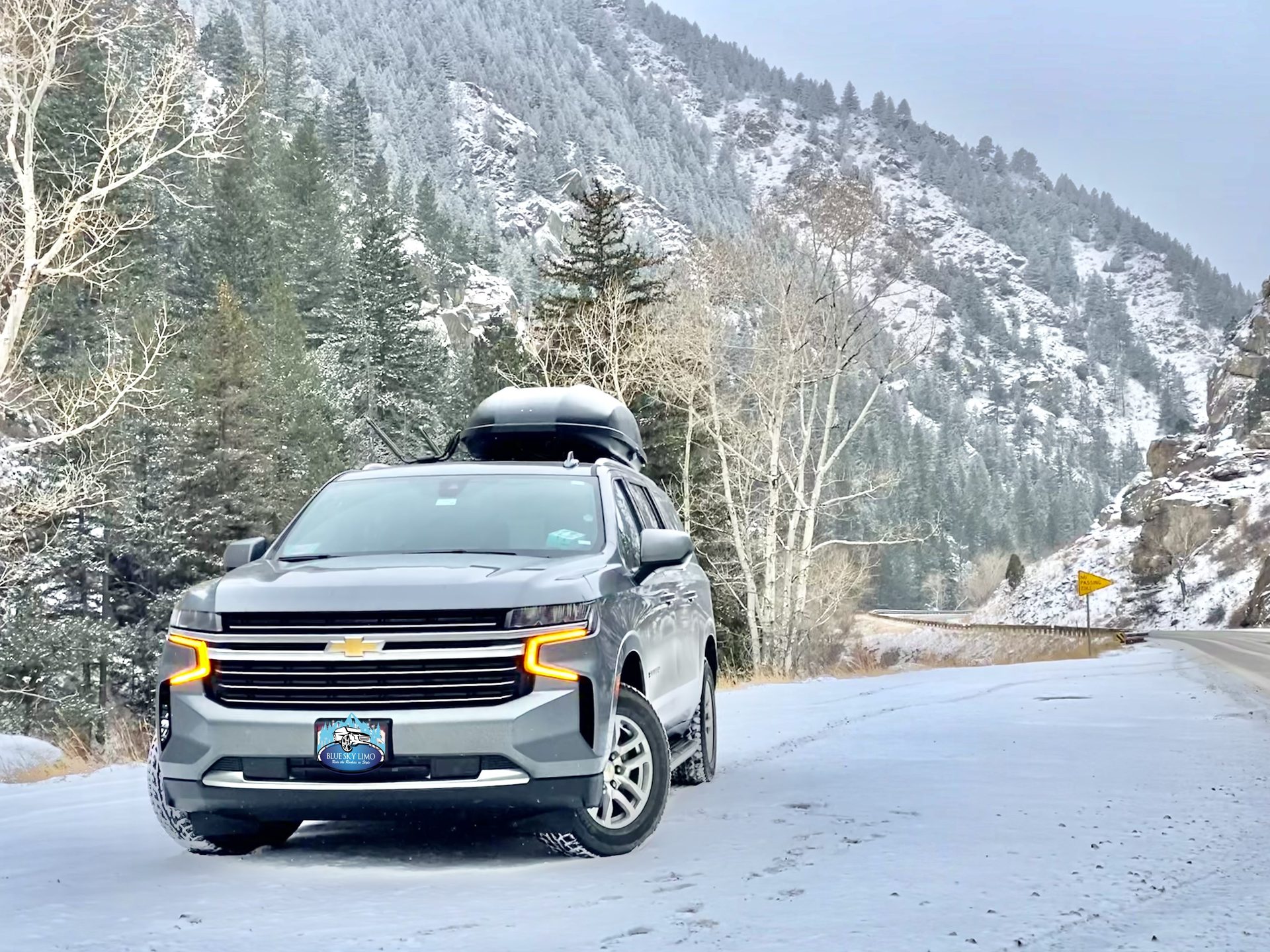Blue Sky Limo Chevrolet Suburban with rooftop cargo box on a snowy Colorado mountain road