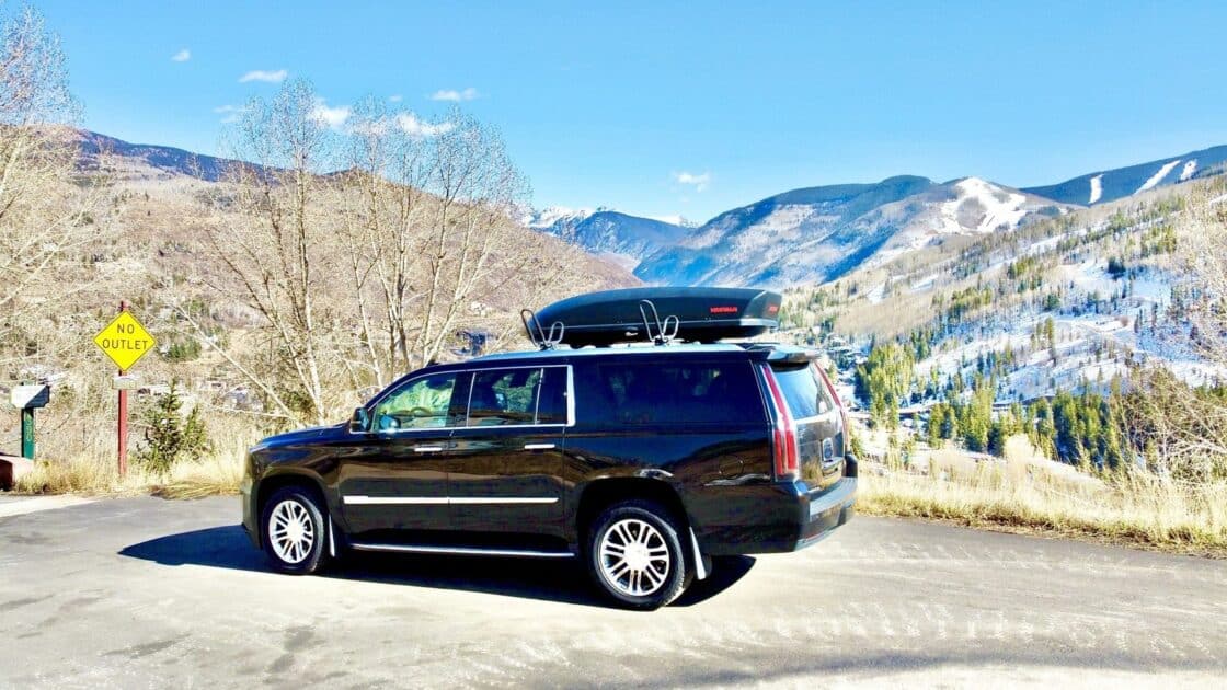 Blue Sky Limo SUV with a rooftop cargo box on a Colorado mountain road